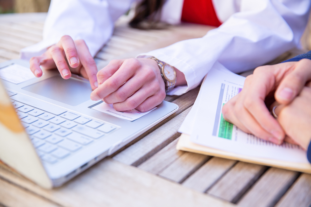 Hands of a medical student using a laptop and hands of a person holding paperwork